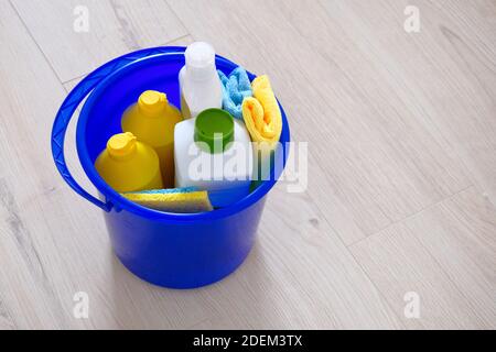 Reinigungsmittel in Plastikflaschen, Schwämme, Pinsel in blauen Haushaltseimer. Hand in gelben Gummihandschuh. Servicekonzept. Speicherplatz kopieren. Stockfoto