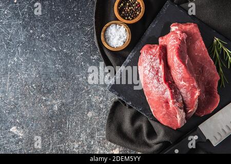 Scheiben rohes Striploin Steak auf einem schwarzen Stein Schneidebrett. Draufsicht. Stockfoto