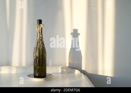 Weinflasche Kerzenhalter mit geschmolzenem Paraffin auf einem Vintage-Weiß Schrank und eine schöne Sonnenreflexion an der Wand - Eine Innenarchitektur und Stil Konz Stockfoto