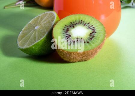 Komposition aus Gläsern mit Orangensaft, Limette, Kiwi und Grün auf hellgrünem Hintergrund Stockfoto