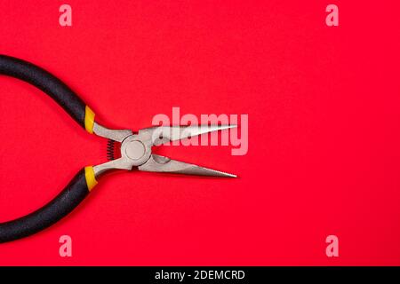 Die Rundzange auf dem roten Hintergrund des Copyspace. Für Elektriker, Juwelier und Baumeister. Metallwerkzeug zum Biegen von Drähten und elektrischen Drähten. Stockfoto