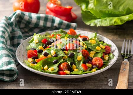 Mexikanischer Salat mit schwarzen Bohnen, Mais, Tomaten, Salat und Pfeffer auf Holztisch Stockfoto