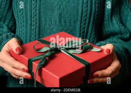Frau hält Weihnachten rotes Geschenk mit grüner Schleife. Weihnachten. Boxtag. Nahaufnahme. Stockfoto
