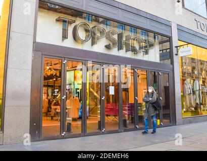 Eine Frau mit einer schützenden Gesichtsmaske geht an Topshop in der Oxford Street vorbei. Viele Unternehmen befinden sich in finanziellen Schwierigkeiten und haben die Schließung angekündigt, da die Coronavirus-Pandemie ihren Tribut für die Wirtschaft fordert. London, Großbritannien, 1. Dezember 2020. Stockfoto