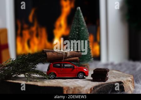 NIS, Serbien - 29. November 2020 Rotes Spielzeugauto mit einem Haufen Baumstümpfe auf dem Dach und Schokoladenwürfeln auf einem Holzbalken zu Hause vor dem kleinen Weihnachtsbaum Stockfoto