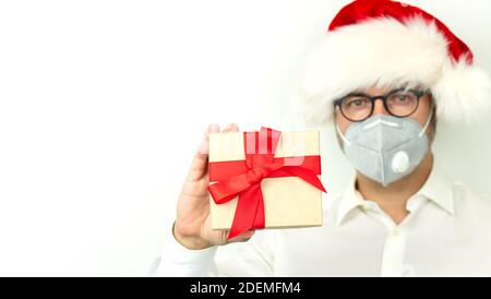 Weihnachten mit Quarantäne und soziale Distanz Konzept, Mann trägt Weihnachtshut und hält Geschenkbox Stockfoto