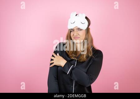 Junge kaukasische Frau trägt Schlafmaske und Schlafanzug über isoliert Rosa Hintergrund mit Schmerzen auf der Schulter und eine schmerzhafte Ausdruck Stockfoto