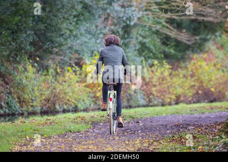 Rückansicht einer isolierten Radfahrerin, die in der Herbstsaison in Großbritannien ihr Fahrrad im Freien reitet und auf einem Landweg radelt. Stockfoto
