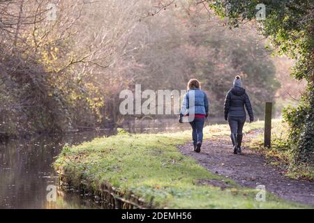 Rückansicht von zwei Frauen, die an einem kalten Morgen zu Winterbeginn isoliert entlang eines britischen Kanals in Worcestershire spazieren gehen, mit Kopierraum links. Stockfoto