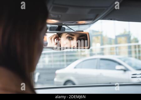 Frau Fixierung Haare beim Blick in Auto Rückspiegel auf Verschwommener Vordergrund Stockfoto