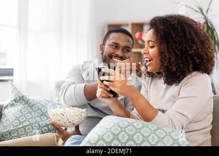 afrikanisches Paar mit Popcorn und Smartphone zu Hause Stockfoto