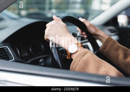 Beschnittene Ansicht der Frau in Armbanduhr Auto fahren auf verschwommen Vordergrund Stockfoto