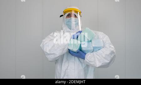 Eine Krankenschwester im Schutzanzug PPE trägt mehrere Pakete neuer Masken in seinen Armen. Der Arzt trägt eine Gesichtsmaske, um Coronavirus zu verhindern. Stockfoto