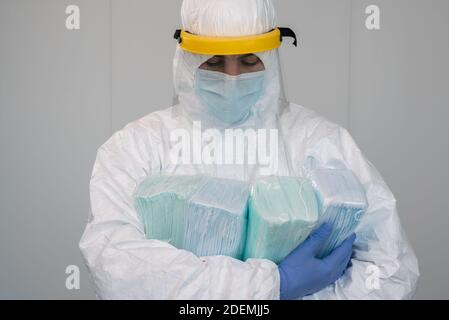 Eine Krankenschwester im Schutzanzug PPE trägt mehrere Pakete neuer Masken in seinen Armen. Der Arzt trägt eine Gesichtsmaske, um Coronavirus zu verhindern. Stockfoto