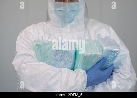 Eine Krankenschwester im Schutzanzug PPE trägt mehrere Pakete neuer Masken in seinen Armen. Der Arzt trägt eine Gesichtsmaske, um Coronavirus zu verhindern. Stockfoto