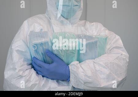 Eine Krankenschwester im Schutzanzug PPE trägt mehrere Pakete neuer Masken in seinen Armen. Der Arzt trägt eine Gesichtsmaske, um Coronavirus zu verhindern. Stockfoto