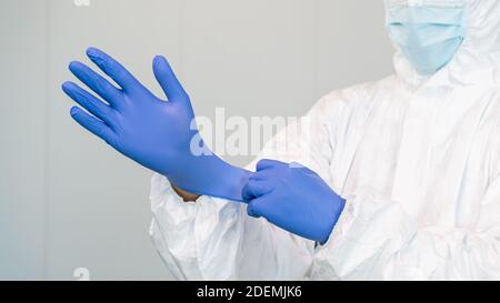 Ein Mitarbeiter des Gesundheitswesens bereitet sich darauf vor, indem er Handschuhe zur Behandlung von kovidierten Patienten aufsetzt. Die Krankenschwester trägt einen Schutzanzug PSA. Coronavirus Stockfoto