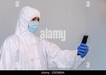 Ein Arzt in PPE Beratung mobile Anwendung auf dem Smartphone während einer Pandemie von covid-19 in einem Krankenhaus von Spanien. Healthcare Worker Telemedizin Konz Stockfoto