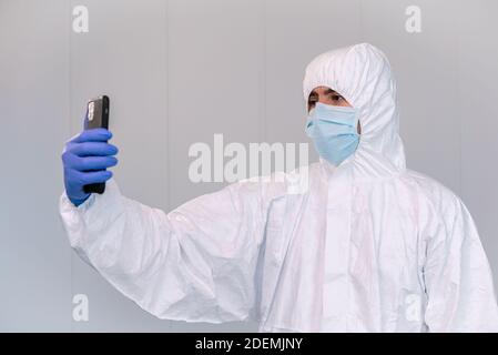 Ein Arzt in PPE Beratung mobile Anwendung auf dem Smartphone während einer Pandemie von covid-19 in einem Krankenhaus von Spanien. Healthcare Worker Telemedizin Konz Stockfoto