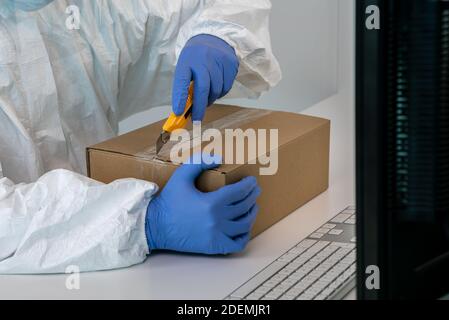 Arzt in Schutzanzug öffnet eine Schachtel mit Gesichtsmasken während Covid19. Mann trägt Handhandschuhe und PSA in der Klinik Einrichtung inmitten Coronavirus. Contami Stockfoto