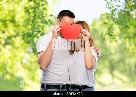 Lächelndes Paar versteckt hinter großen roten Herzen Stockfoto