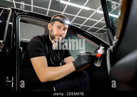 Professionelle männliche Auto-Service-Arbeiter in schwarzen Uniform und Schutzhandschuhe, führt eine Reinigung der Tür des modernen Fahrzeugs mit Reinigungsschaum Stockfoto