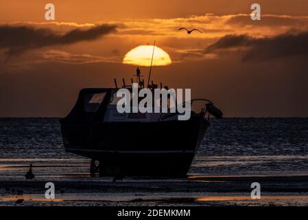 Sonne geht hinter einem festgemachtes, beachtes Boot in der Morgendämmerung auf, Sonnenaufgang am ersten Tag des meteorologischen Winters, Dezember 2020 in Southend on Sea, Essex, UK Stockfoto