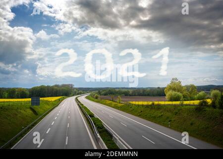 Leere Autobahn führt durch eine ländliche Landschaft zum Neujahr Nummer 2021 geschrieben in den wolkigen Himmel, kopieren Raum Stockfoto