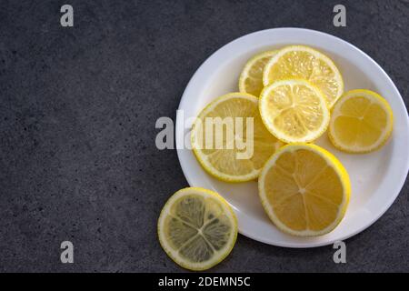 Zitronenscheiben auf weißem Teller. Grauer Hintergrund mit Kopierbereich. Stockfoto