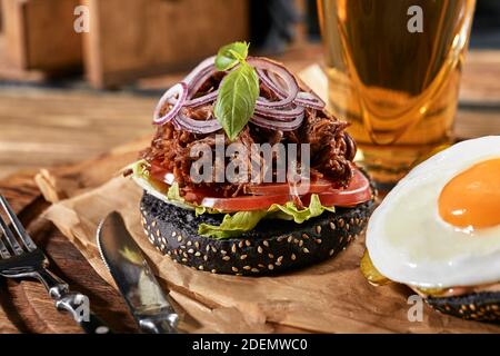 Guter Burger, mit Rindfleisch, Zwiebeln, süßen Zwiebeln, Käse, Salat, Tomaten auf Bastelpapier mit einem Glas Bier auf dem Hintergrund. Stockfoto