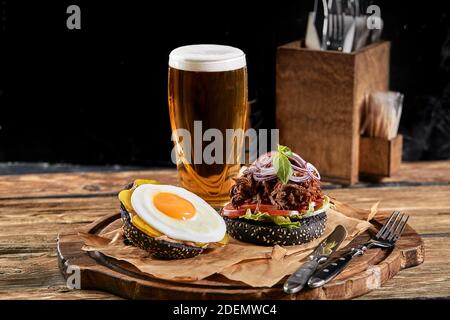 Guter Burger, mit Rindfleisch, Zwiebeln, süßen Zwiebeln, Käse, Salat, Tomaten auf Bastelpapier mit einem Glas Bier auf dem Hintergrund. Stockfoto