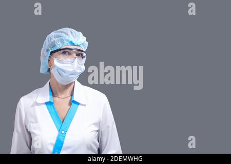 Krankenschwester in Schutzbrille, Hut und Maske steht drehen den Kopf nach links auf einem grauen Hintergrund, kopieren Raum nach rechts, das Konzept der Medizin in Th Stockfoto