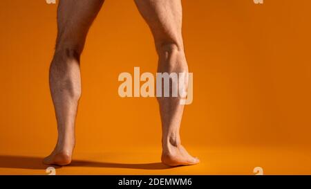 Muskulöse Männerbeine in Hocke, schwingen Beinmuskeln, Übung. Körperteile, gelber Hintergrund. Stockfoto