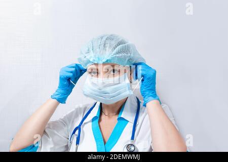 Krankenschwester in einer Kappe und Gummihandschuhe legt auf eine medizinische Maske, auf einem hellen Hintergrund, das Konzept des Schutzes gegen Coronovirus-Infektion Stockfoto