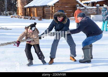 Irkutsk, Russland - 8. Januar 2019: Glückliche Menschen, die Spaß am Tauziehen im Park des Museums Taltci haben. Zwei Männer und ein Junge ziehen an einem Seil Stockfoto