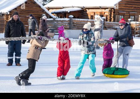 Irkutsk, Russland - 8. Januar 2019: Glückliche Familien mit Kindern, die Spaß am Tauziehen im Winterpark des Ethnographischen Museums Taltci haben. Stockfoto