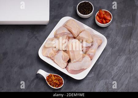 Rohes Huhn zartes Curry mit Haut auf weiß angeordnet geschnitten Teller und mit schwarzem Pfeffer und Tomatenscheiben garniert Hintergrund in Graphitfarbe Stockfoto