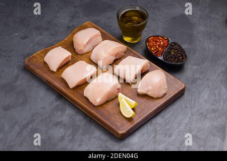 Rohes Huhn zart braten geschnitten ohne Haut auf Holz angeordnet Mit Öl, Zitronenscheiben, kalten Flocken und schwarzem Pfeffer garniert Auf grauem Hintergrund Stockfoto