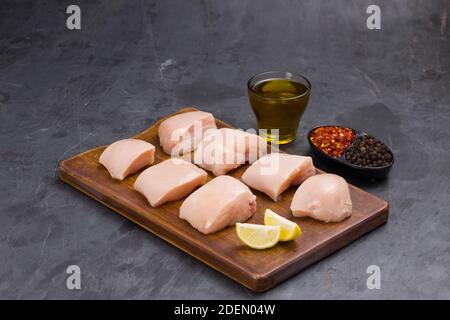 Rohes Huhn zart braten geschnitten ohne Haut auf Holz angeordnet Mit Öl, Zitronenscheiben, kalten Flocken und schwarzem Pfeffer garniert Auf grauem Hintergrund Stockfoto