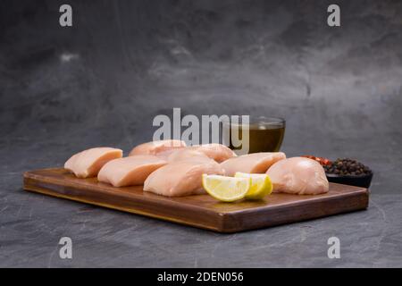 Rohes Huhn zart braten geschnitten ohne Haut auf Holz angeordnet Mit Öl, Zitronenscheiben, kalten Flocken und schwarzem Pfeffer garniert Auf grauem Hintergrund Stockfoto