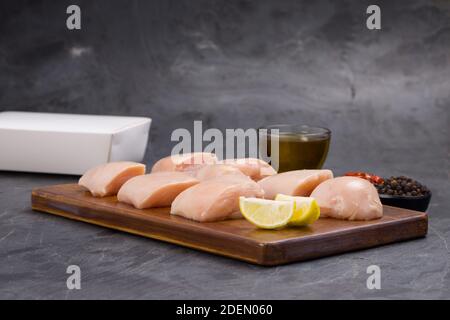 Rohes Huhn zart braten geschnitten ohne Haut auf Holz angeordnet Mit Öl, Zitronenscheiben, kalten Flocken und schwarzem Pfeffer garniert Auf grauem Hintergrund Stockfoto