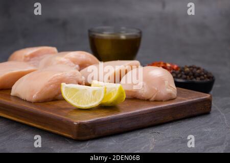 Rohes Huhn zart braten geschnitten ohne Haut auf Holz angeordnet Mit Öl, Zitronenscheiben, kalten Flocken und schwarzem Pfeffer garniert Auf grauem Hintergrund Stockfoto