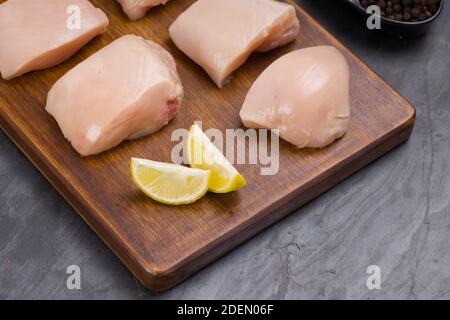 Rohes Huhn zart braten geschnitten ohne Haut auf Holz angeordnet Mit Öl, Zitronenscheiben, kalten Flocken und schwarzem Pfeffer garniert Auf grauem Hintergrund Stockfoto