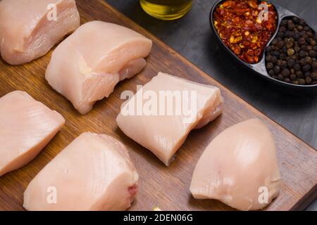 Rohes Huhn zart braten geschnitten ohne Haut auf Holz angeordnet Mit Öl, Zitronenscheiben, kalten Flocken und schwarzem Pfeffer garniert Auf grauem Hintergrund Stockfoto