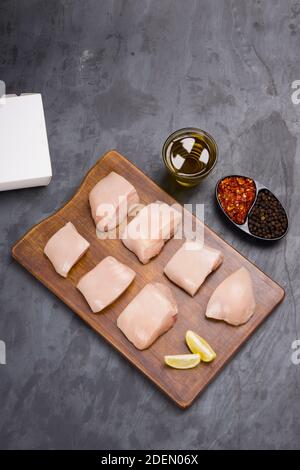 Rohes Huhn zart braten geschnitten ohne Haut auf Holz angeordnet Mit Öl, Zitronenscheiben, kalten Flocken und schwarzem Pfeffer garniert Auf grauem Hintergrund Stockfoto