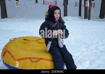 Fröhlicher schöner Junge Reiter der Achterbahn. Kleinkind Wandern im Schnee im Winter. Das Kind lacht und lächelt in Winter Park. Stockfoto