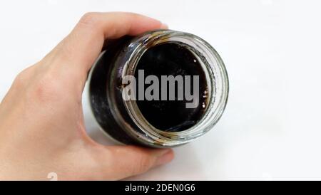 Eine Hand, die ein Glas mit schwarzem Gelee hält, ohne Deckel. Blick von oben. Stockfoto