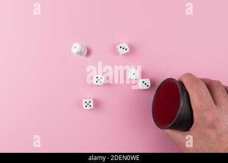 Direkt über Ansicht des Spielers Wurf oder Würfeln mit Ein Würfelschüttler vor rosa Hintergrund Stockfoto