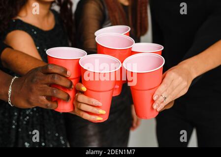 Taille bis von sechs Freunden Spaß und Alkohol trinken während der Neujahrsparty, isoliert auf weißem Hintergrund. Eine Gruppe von fröhlichen Freunden verschiedener Nationalitäten klirrt auf einer Party im Studio auf eine Brille mit roten Gläsern. Stockfoto