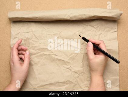 Leeres zerrissenes Blatt braunes Bastelpapier und zwei Hände mit schwarzem Holzstift, Holztisch, Draufsicht, Platz für eine Inschrift Stockfoto